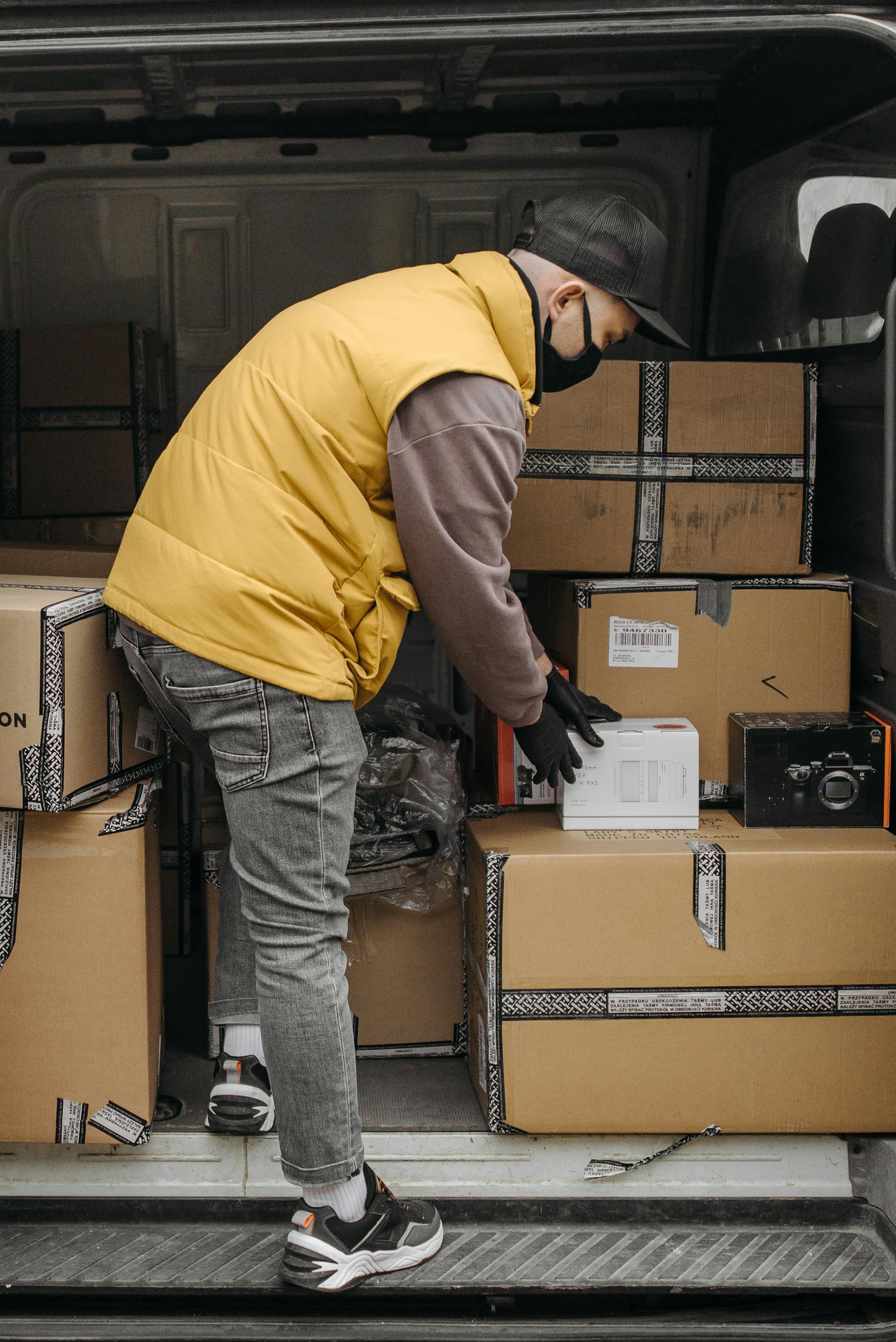 A delivery person organizing packages in a van, wearing a facemask for safety.